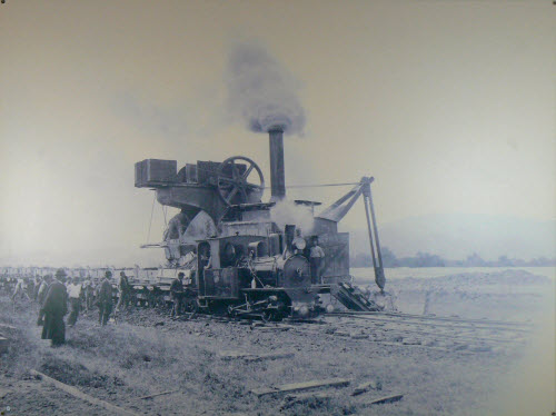 Trockeneimerkettenbagger mit Holzkastenkipper der IRR-Dienstbahn und der Dampflokomotive Rhein