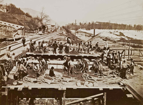 Fundationsarbeiten im Winter zur Überleitung vom Werdenberger Binnenkanal in den Rheintaler Binnenkanal Schluuch; Arbeiter mit Schubkarren und Schaufeln, Dienstbahn und Kanal sichtbar, in der Mitte die Rheintalstrecke der SBB